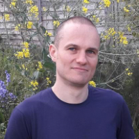 Portrait of Marcos Patchett in a garden. Yellow and purple flowers behind him