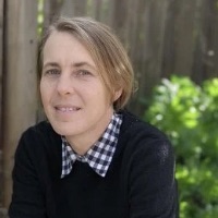 Portrait of Stevie Lowe outside, sunlight dappled on green leaves